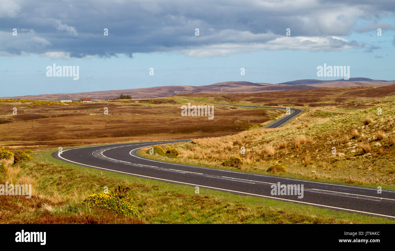 Panoramic landscape of vast golden moors in highlands of Scotland with narrow road leading to distant mountains under blue sky Stock Photo