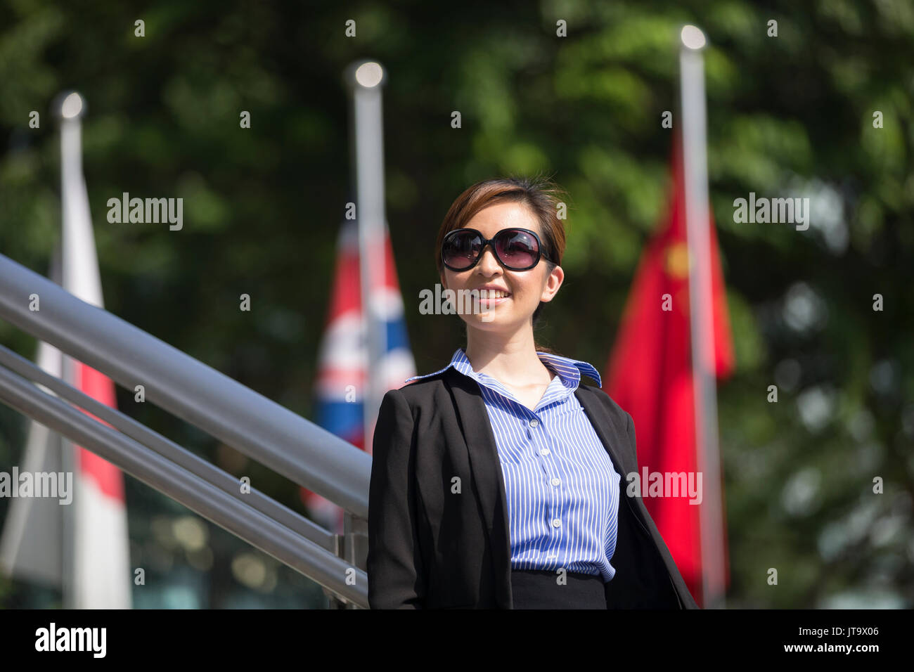Indian business woman with a Smart Phone, in front of flags. Portrait of an Asian businesswoman smiling, holding a Smart Phone, in front of flags. Glo Stock Photo