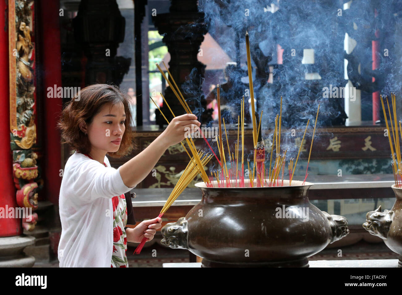 Buddhist worshipper placing incense sticks on joss stick pot hires