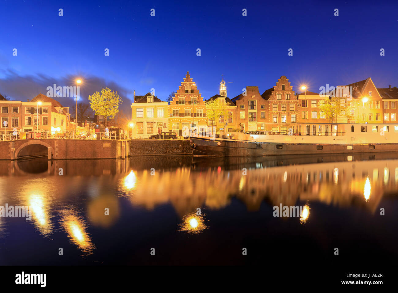 Dusk lights on typical houses and bridge reflected in a canal of the River Spaarne, Haarlem, North Holland, The Netherlands Stock Photo