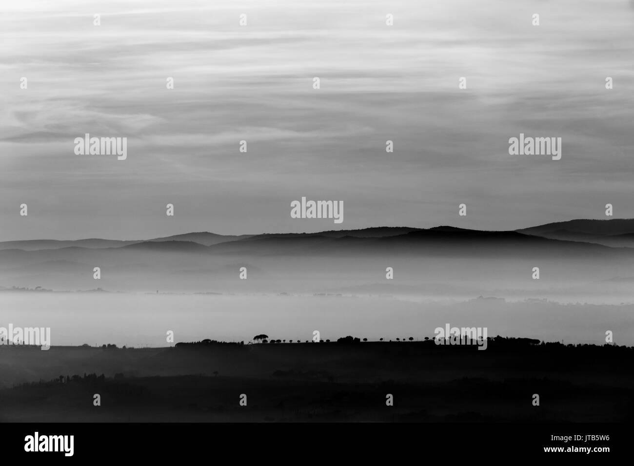 A view of some trees on top of a hill with a background of fog and distant mountains Stock Photo