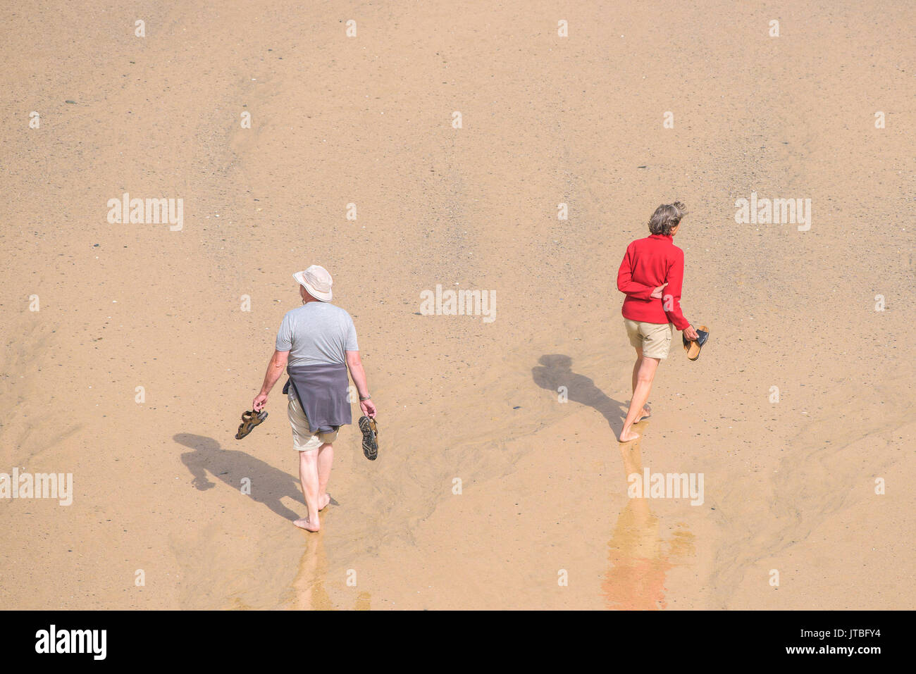 A couple walking barefoot across a beach at low tide. Newquay, Cornwall. Stock Photo