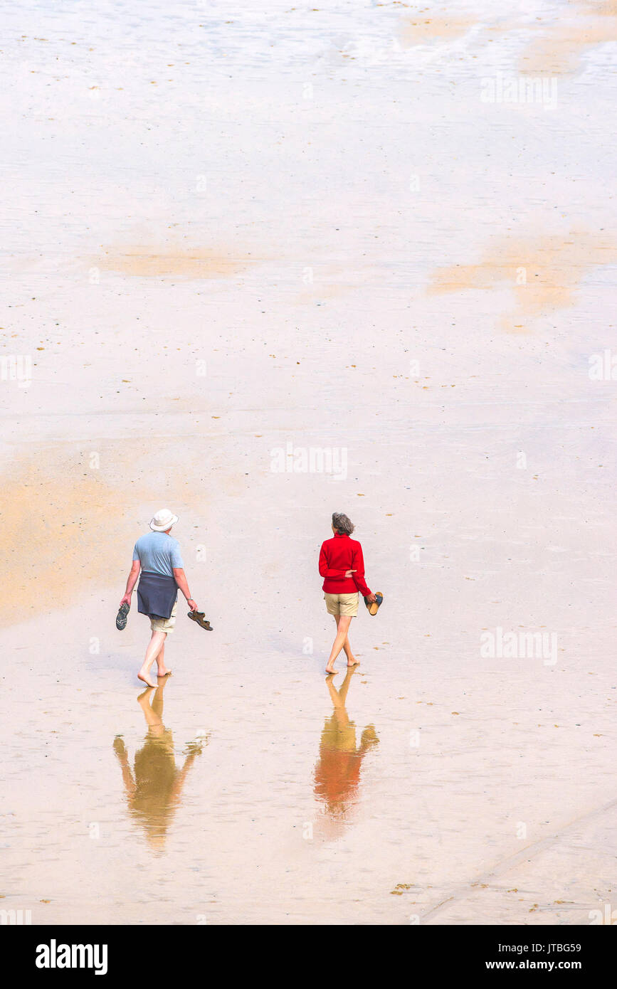 A couple walking barefoot across a beach at low tide. Newquay, Cornwall. Stock Photo