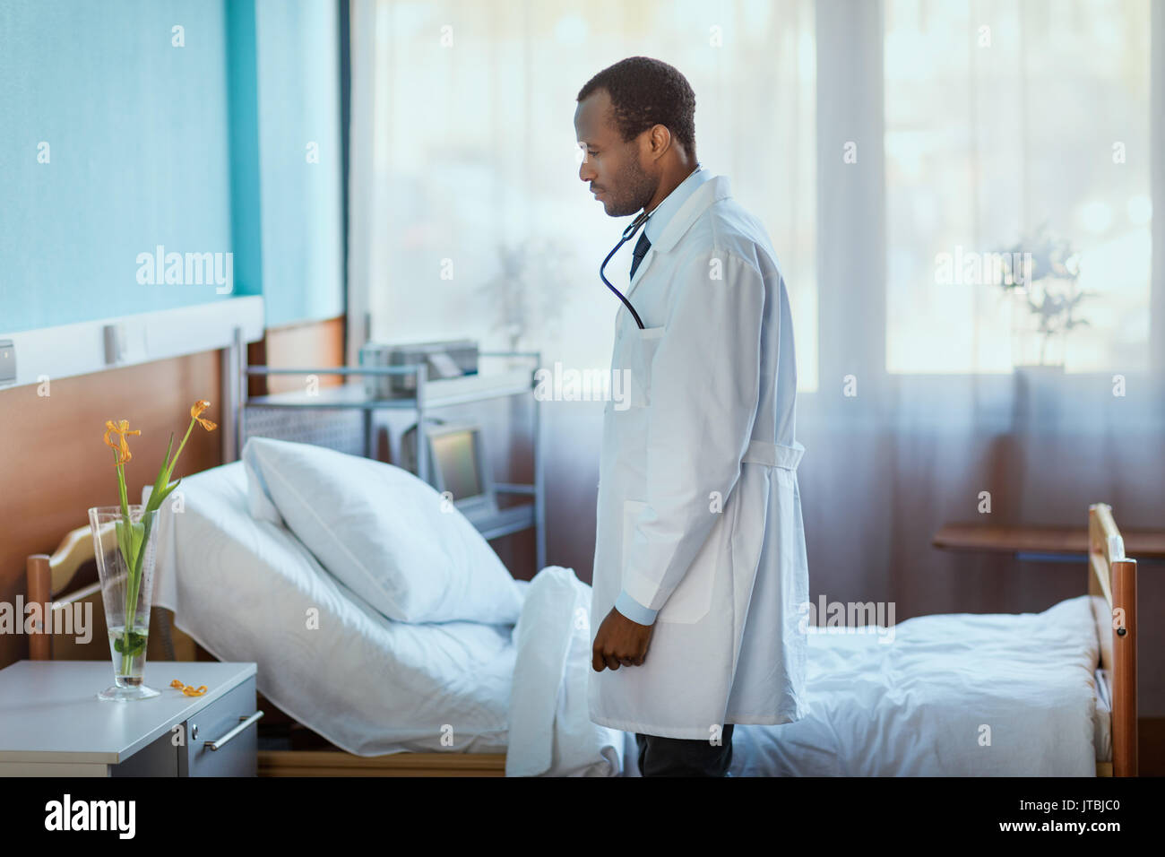 side view of doctor standing near hospital bed and looking at flowers