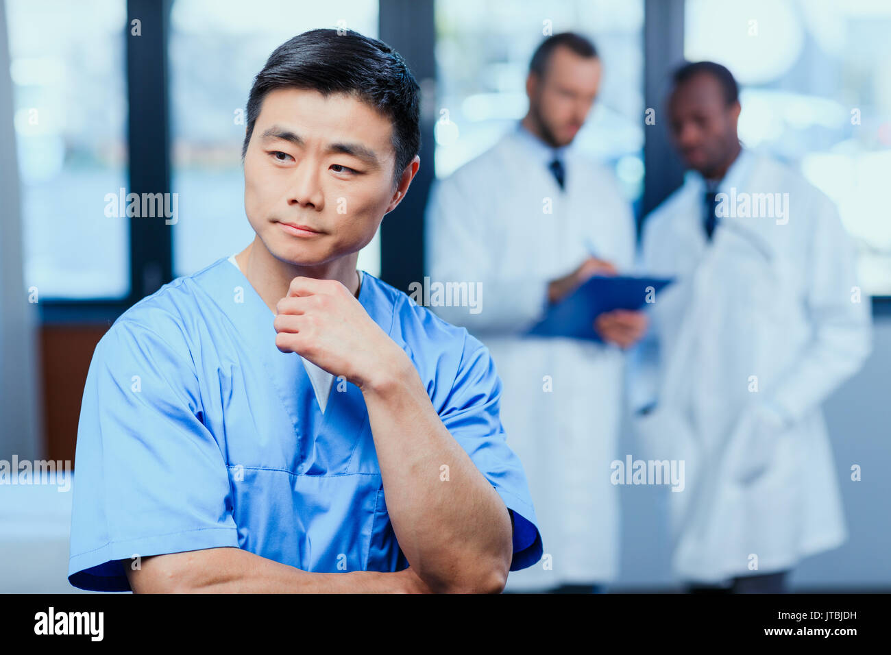 portrait of pensive doctor in medical uniform with collegues behind in clinic Stock Photo