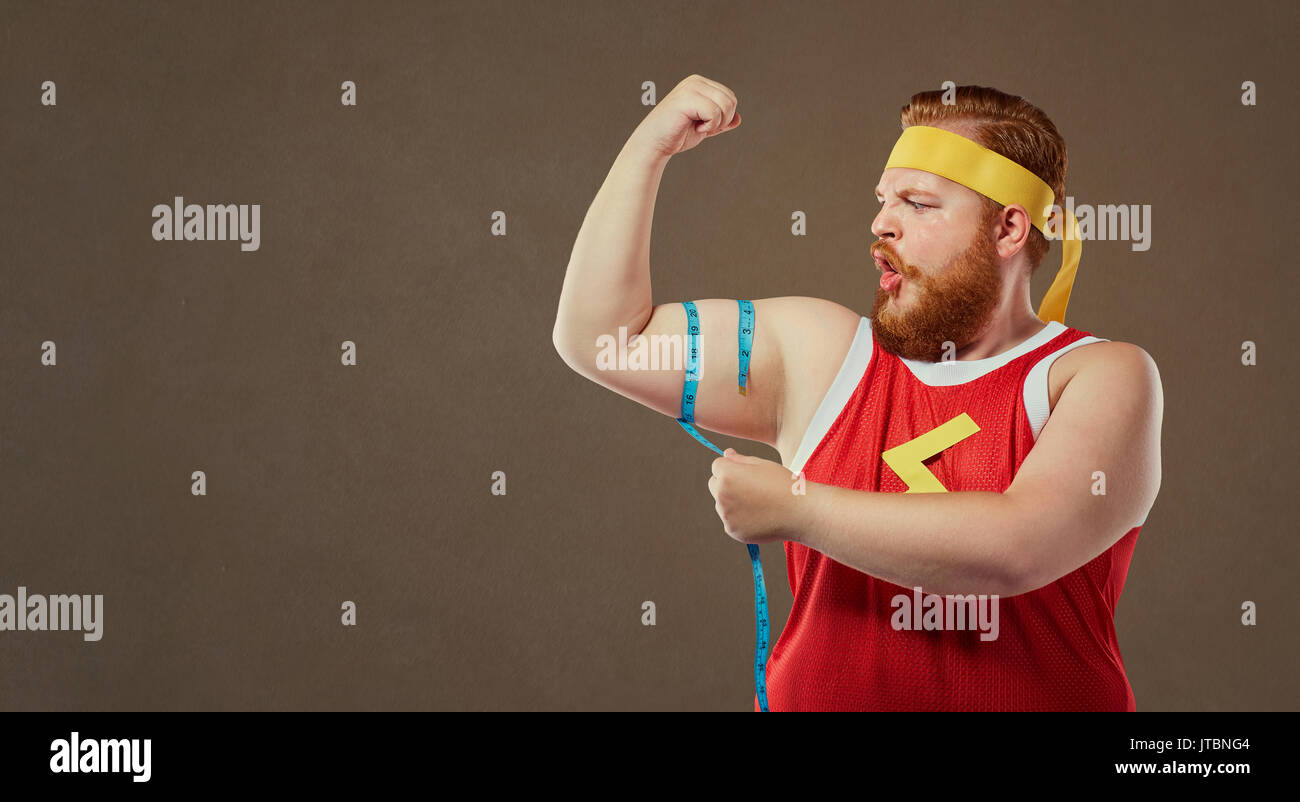 A funny fat man in sports clothes measures his arm with a centim