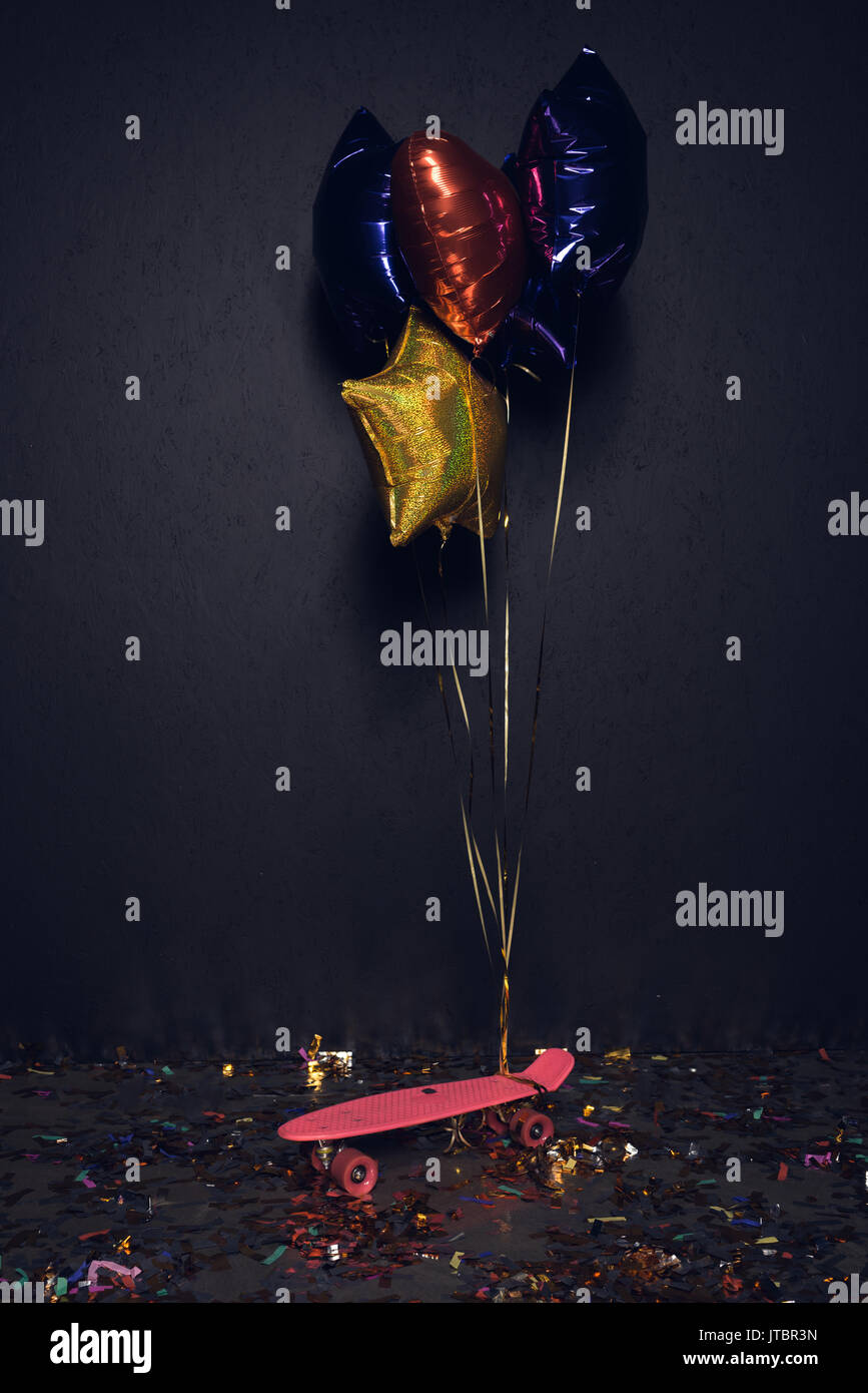 pink skateboard and colorful balloons on floor with confetti at party