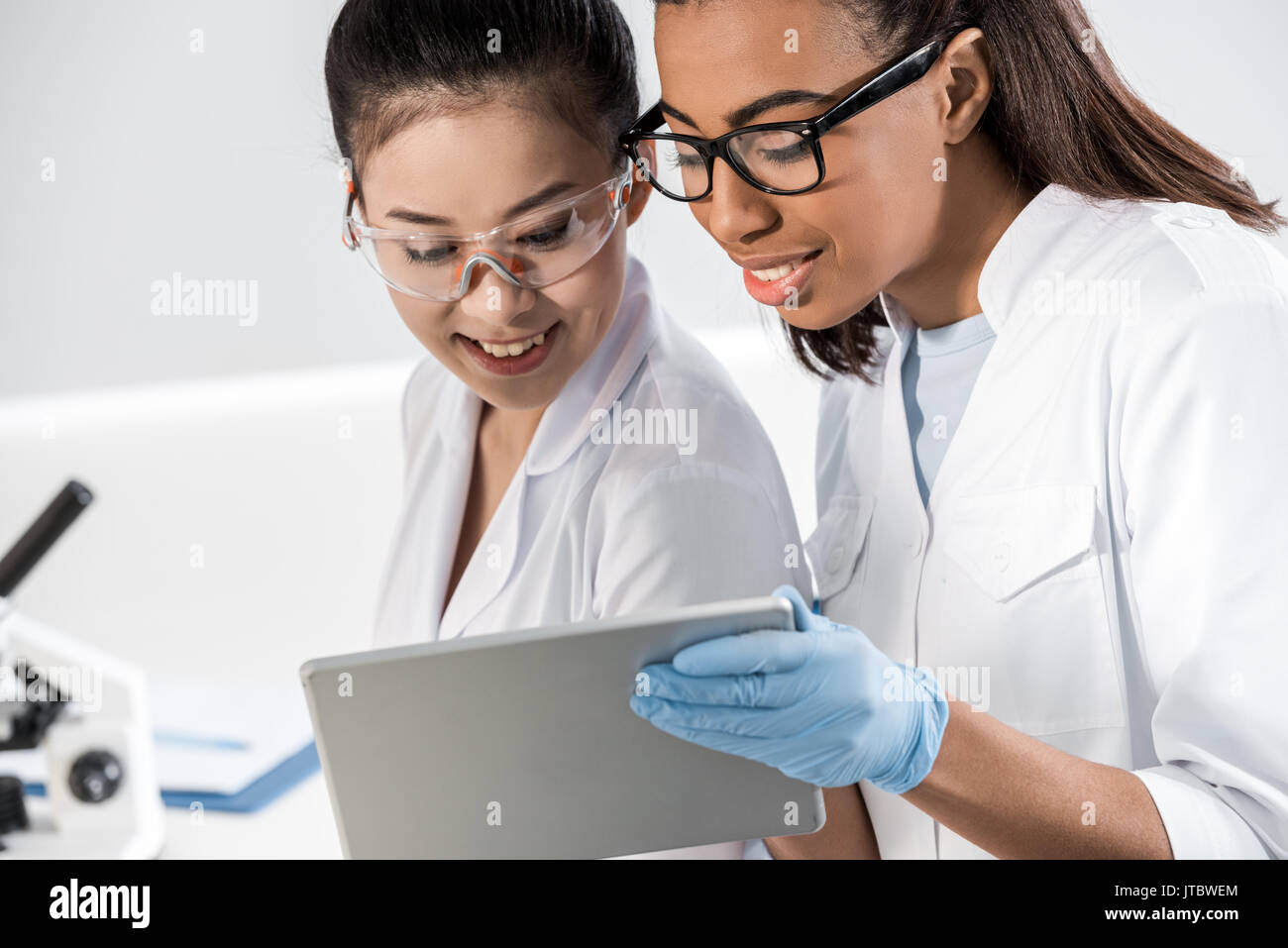 Smiling young scientists in eyeglasses using digital tablet in laboratory, scientists working together Stock Photo