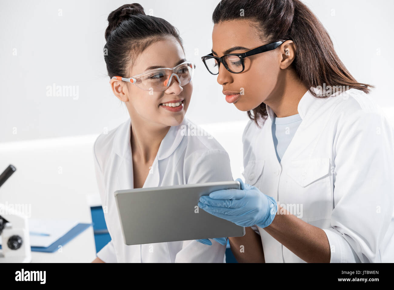 Smiling young scientists in eyeglasses using digital tablet in laboratory, scientists working together Stock Photo