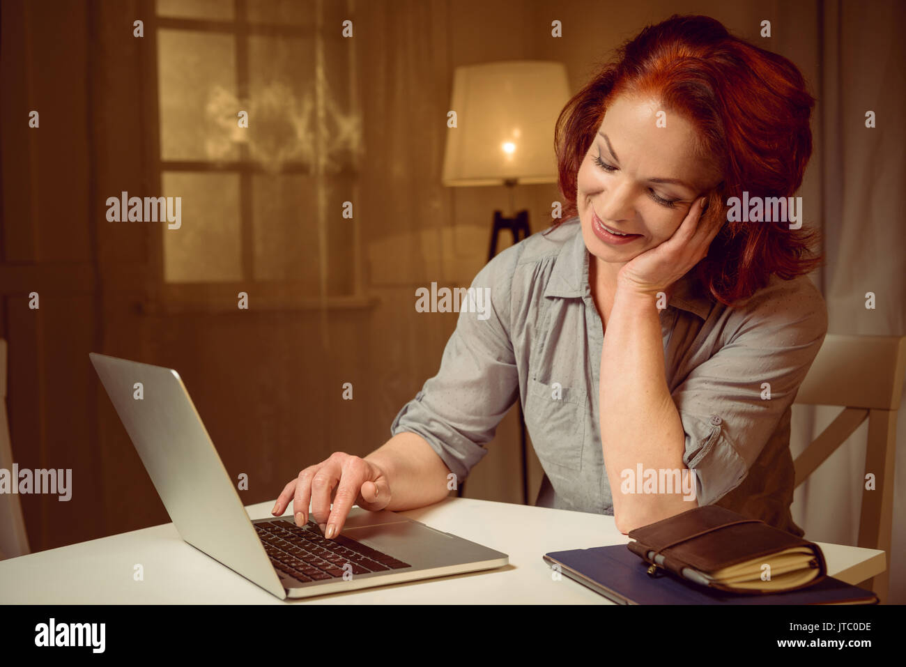 mature red hair woman working on laptop while sitting at table at home Stock Photo