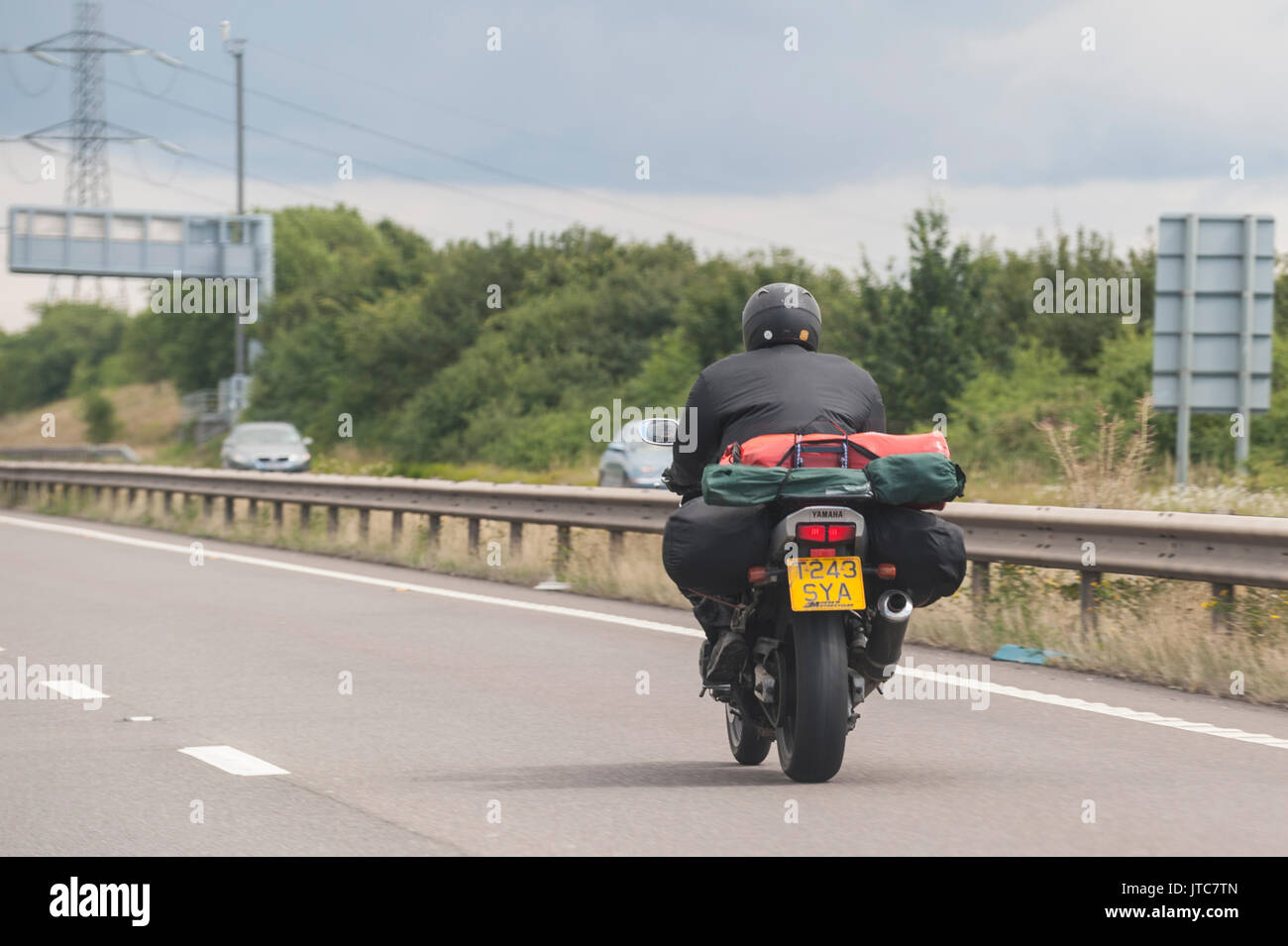 A motorbike with camping gear driving on a main road in the Uk Stock