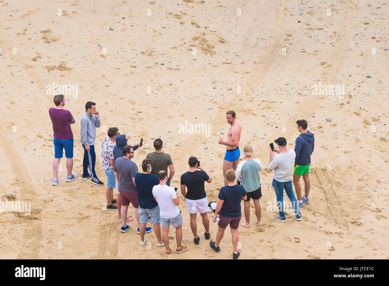 A man wearing blue Calvin Klein underpants and his friends on a beach in Newquay, Cornwall. Stock Photo