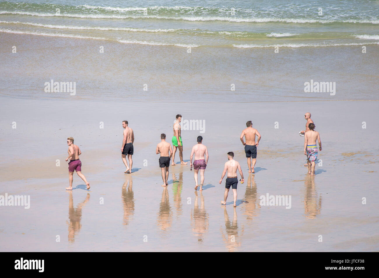 A group of male holidaymakers walking to the sea on Great Western Beach in Newquay, Cornwall. Stock Photo