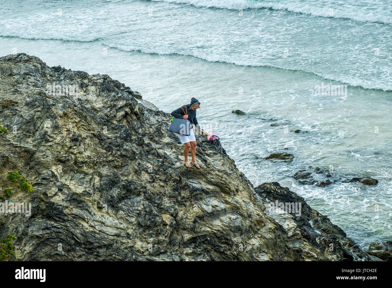 A woman climbing down slippery rocks at Godrevy Beach in Cornwall. Stock Photo