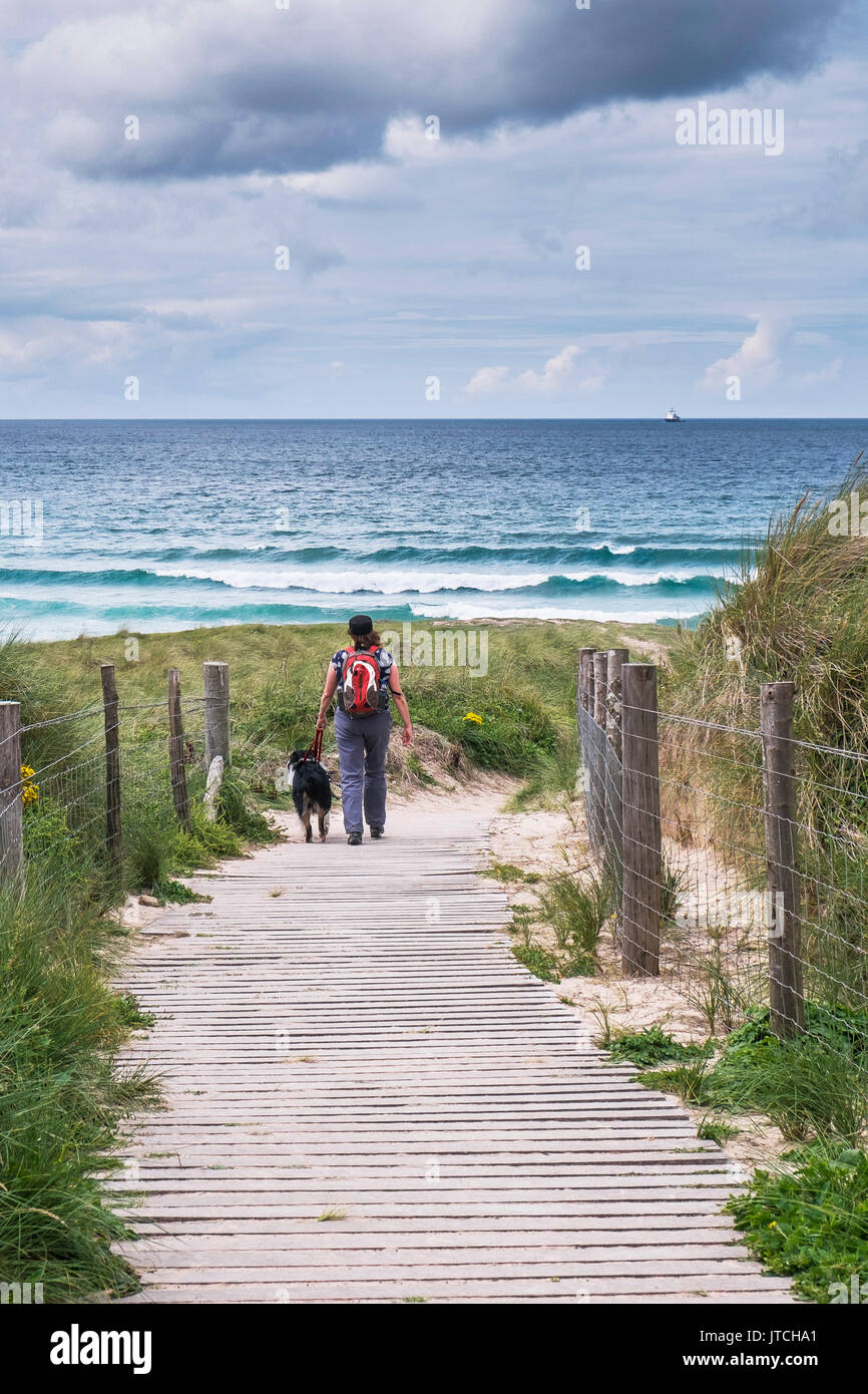 A woman walking her dog on a footpath leading down to the sea. Stock Photo