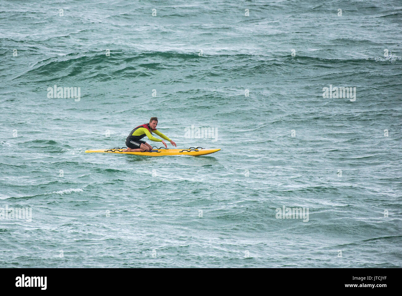 A RNLI lifeguard paddling on his rescue surf board. Stock Photo