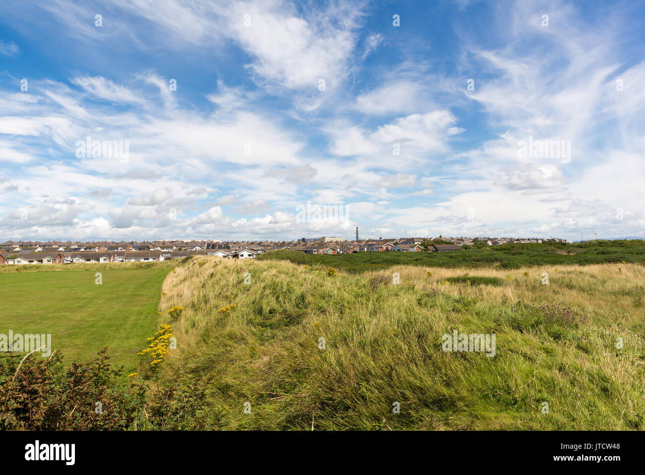 Looking across fields and the rooftops of Vickerstown, Walney Island, Barrow-in-Furness, Cumbria, UK towards BAE Systems submarine hangers. Stock Photo