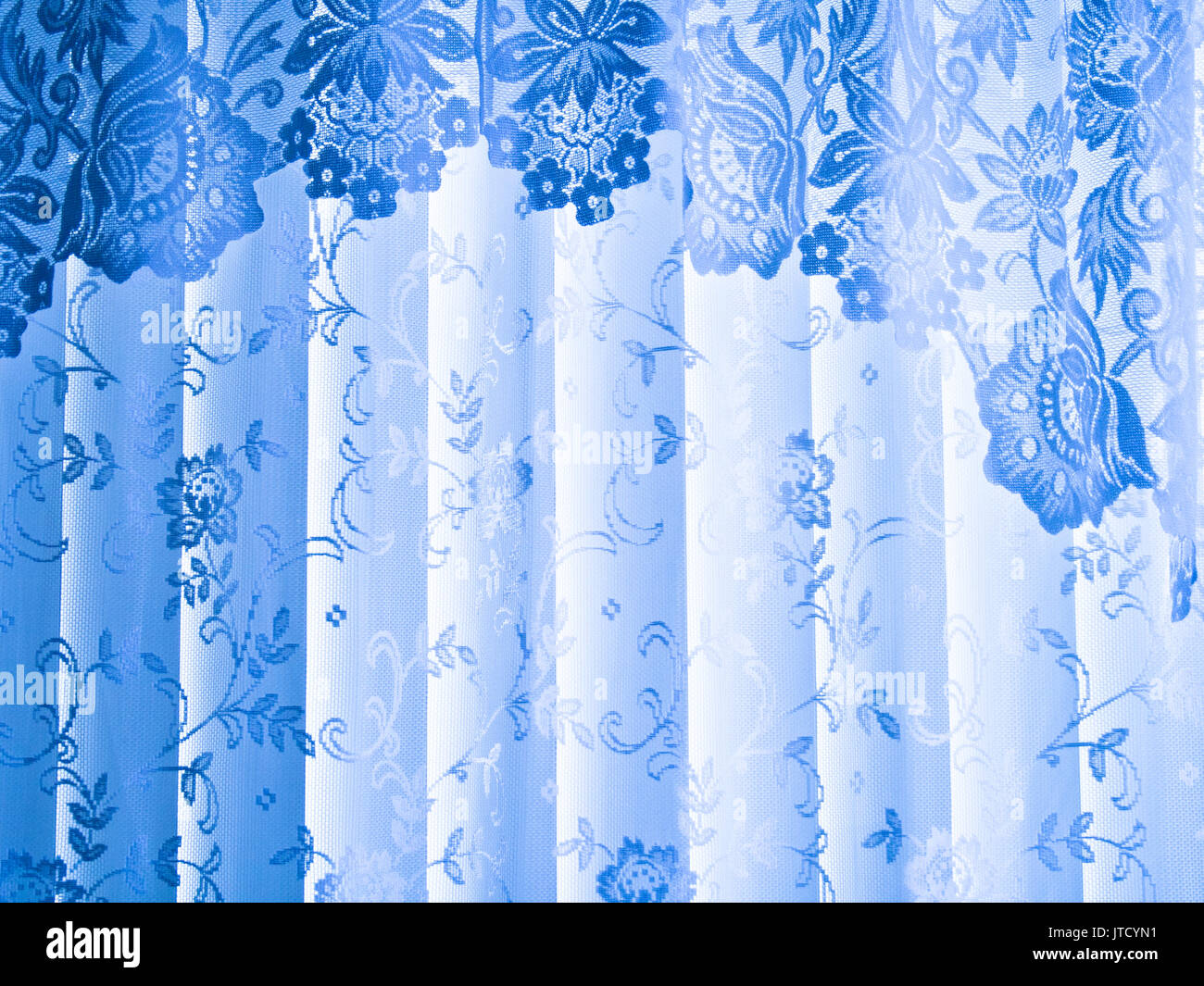Soft, lacy folds of a light blue curtain are topped with a swag valance. Stock Photo