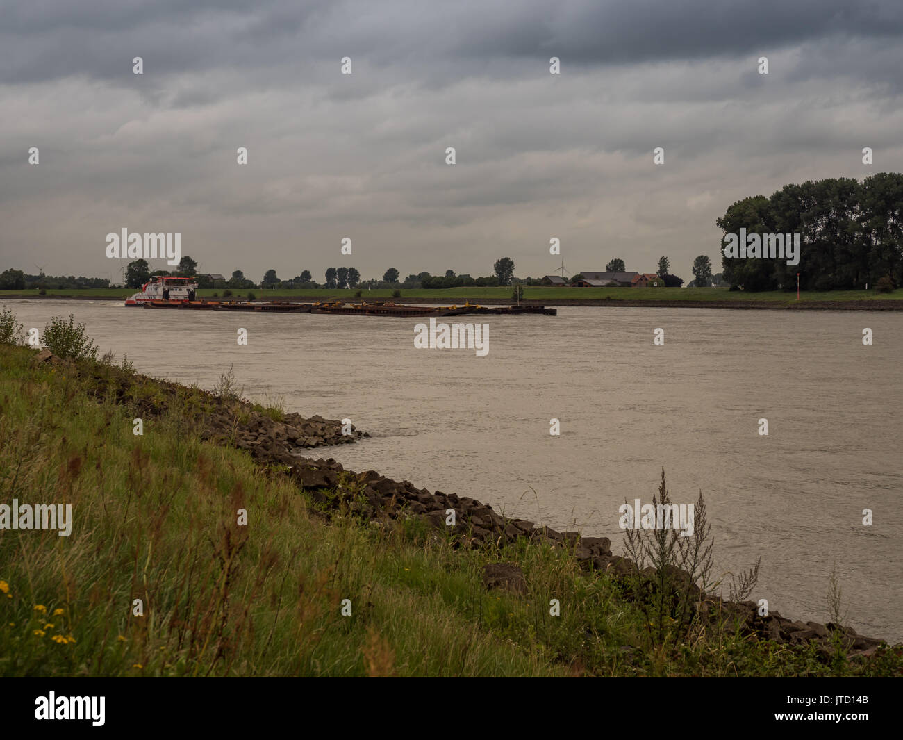 big pushing ship drives upstream the rhine, Grieth am Rhein, Germany on a very cloudy day Stock Photo