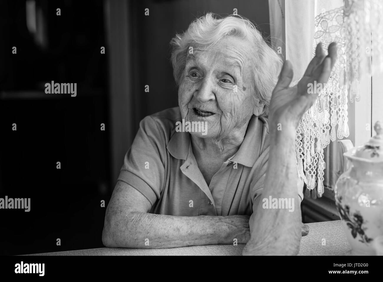 Black-and-white portrait of an elderly woman emotional says in her home. Stock Photo