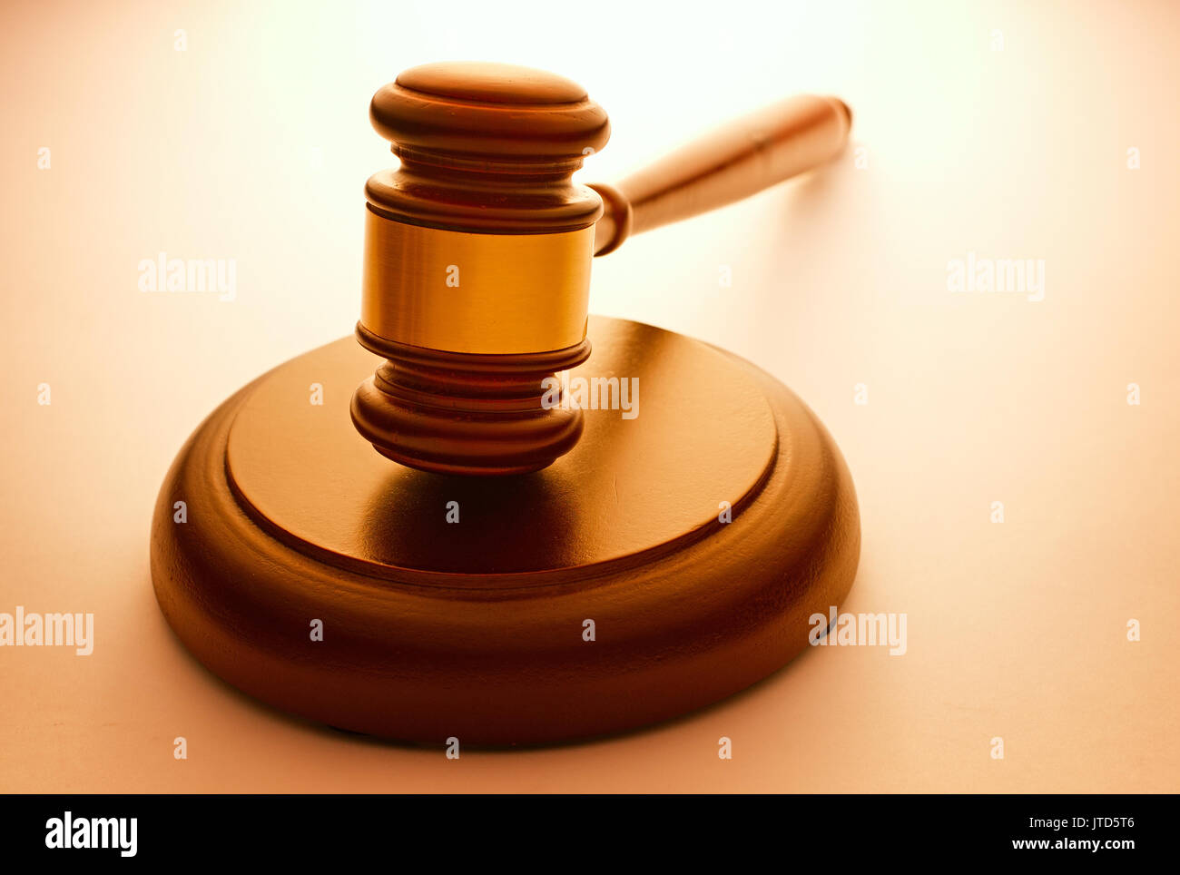 Wooden gavel with a brass band resting on a plinth used by a judge or auctioneer and conceptual of justice and judgements with backlit highlight and c Stock Photo