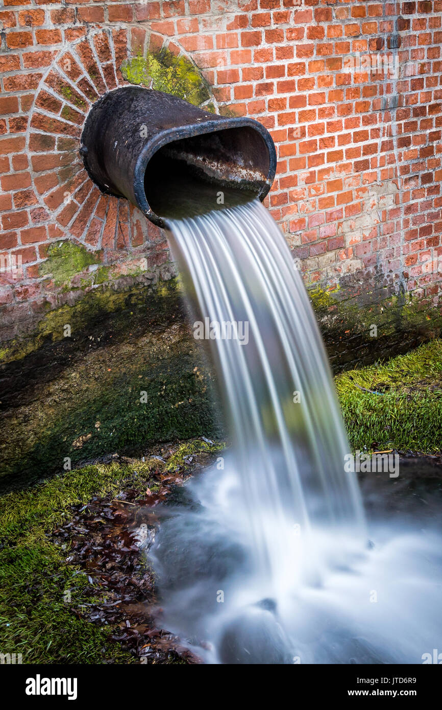 Water cascading from metal pipe mounted in brick wall on green moss Stock Photo