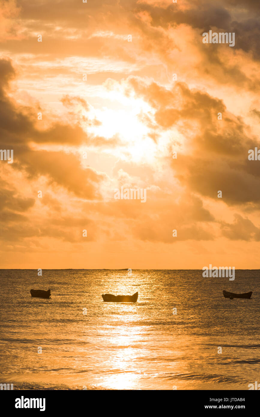 Dhow boat silhouetted in early morning sunlight breaking through clouds over Indian ocean, Diani, Kenya Stock Photo