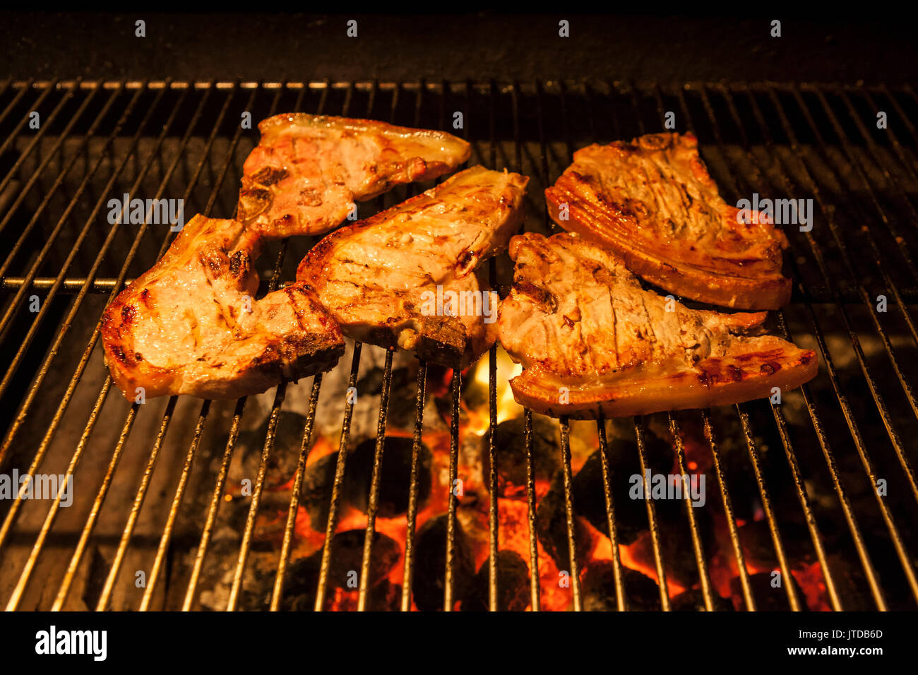 Pork chops on the bone, marinated in lemon juice, sizzling on an openfire charcoal barbeque
