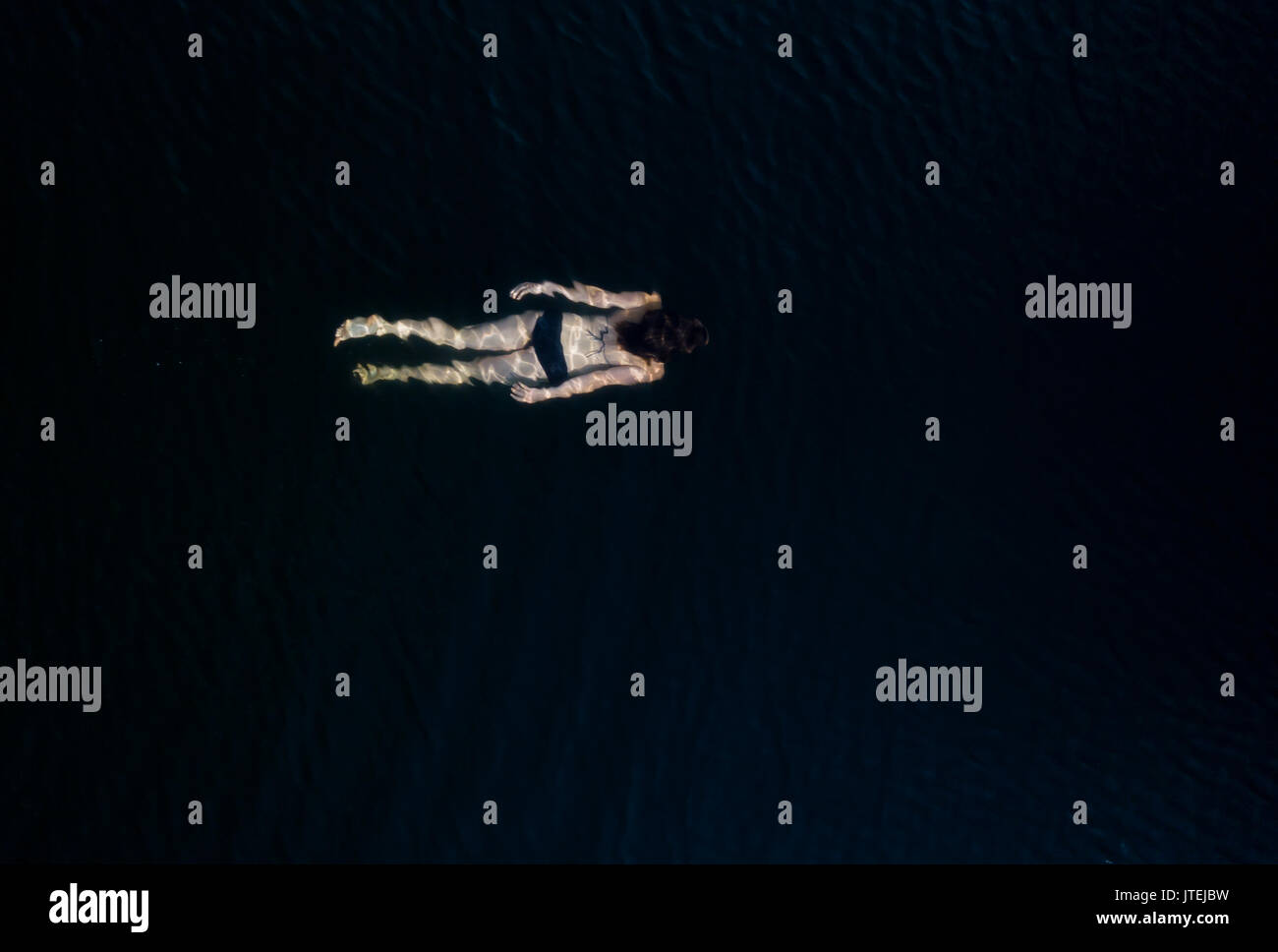 Young female in bikini swimming underwater in dark water Stock Photo ...
