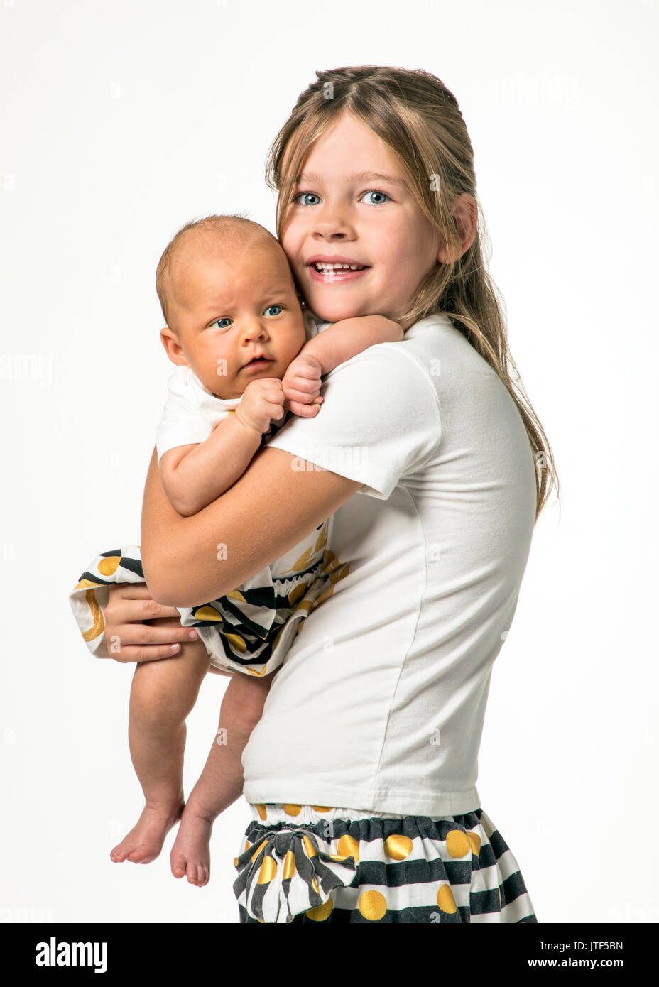 Studio portrait of 7 year old girl holding 7 week old baby Stock Photo