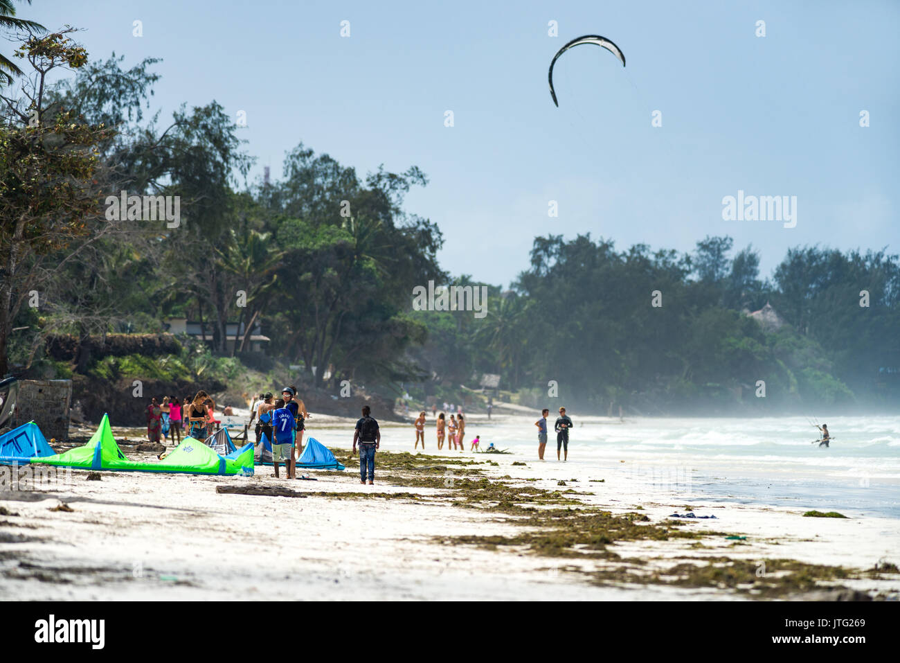 Tourists and locals on beach with kite surfer equipment, Diani, Kenya Stock Photo