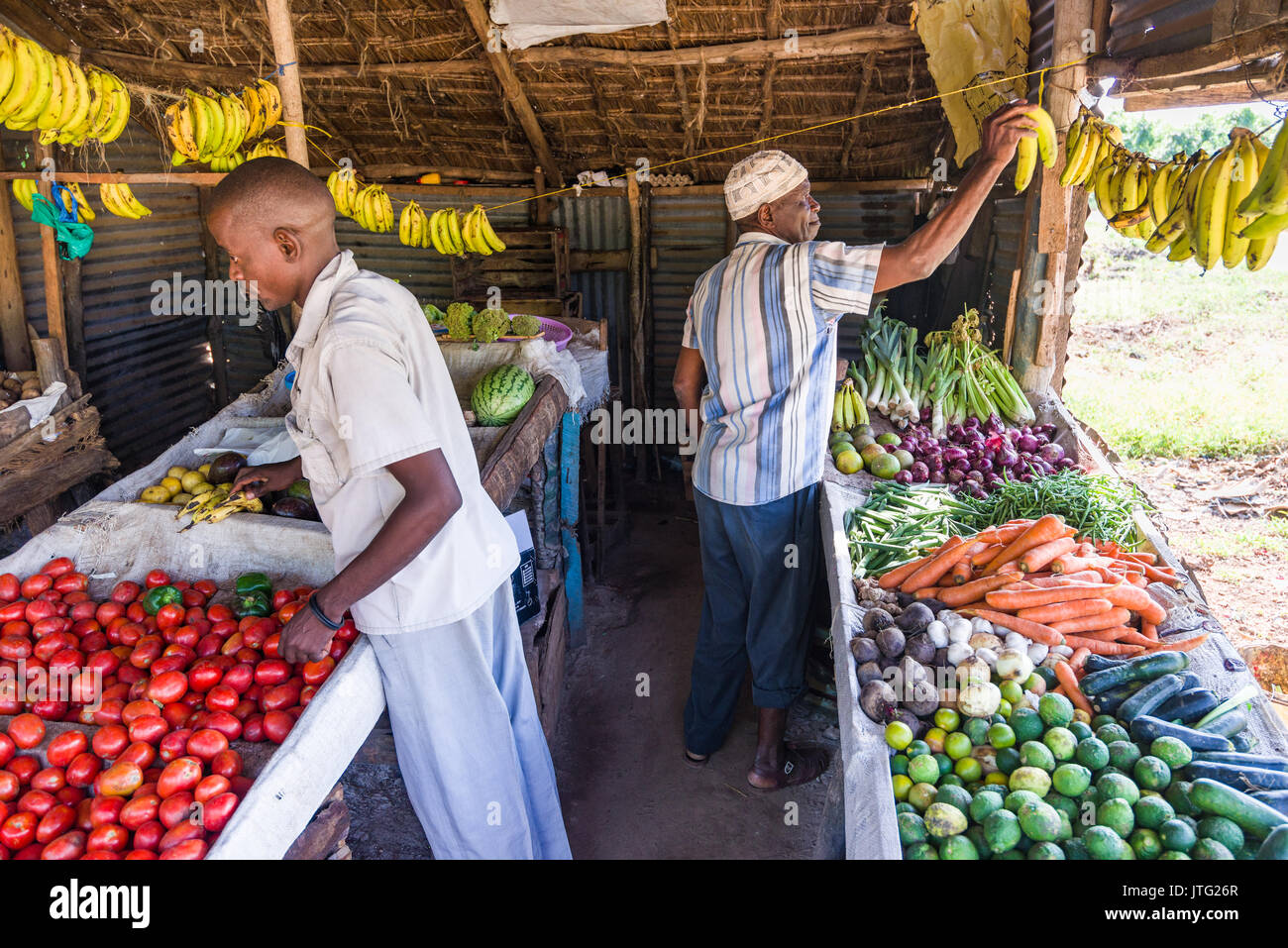 Two local Kenyan men in small fresh fruit and vegetable stall browsing