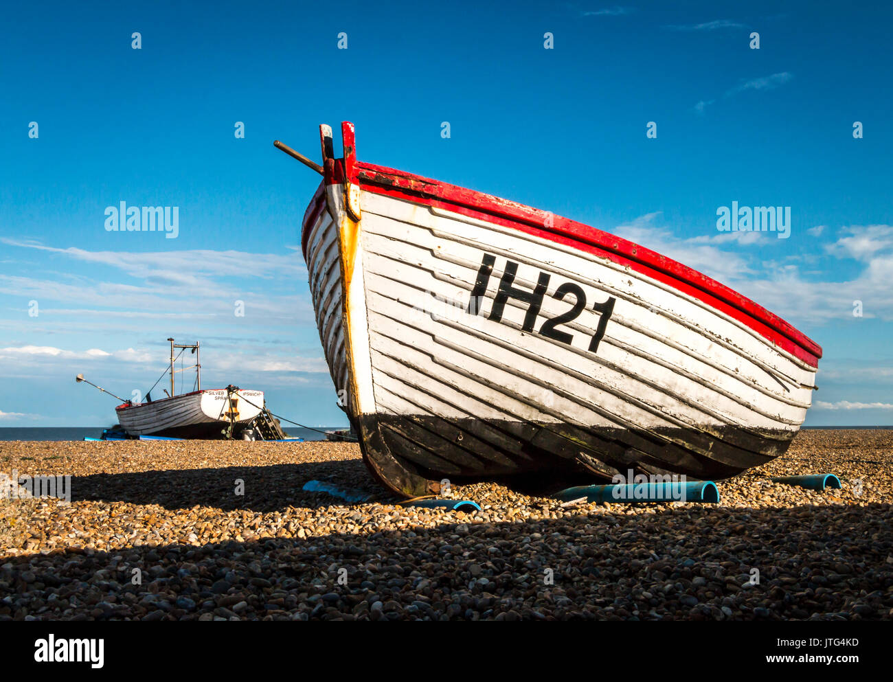 Historic wooden fishing boats sitting in the summer sun on the shingle beach at Aldeburgh on the Suffolk coast in the UK. Stock Photo