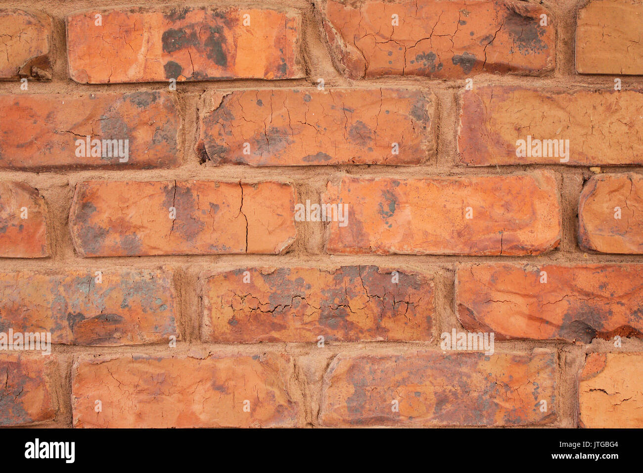 A closeup of irregular shaped red bricks layered in a horizontal pattern with orange brown mortar used to bind them together to construct a brick wall. Stock Photo