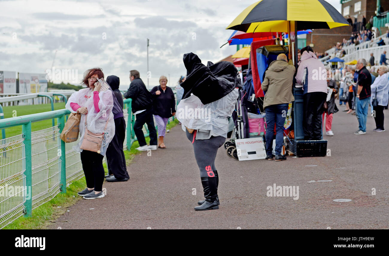 Brighton, UK. 9th Aug, 2017. This racegoer has trouble with her coat in the wind and rain at the Marstons Race Day in the Maronthonbet Festival of Racing at Brighton Racecourse Credit: Simon Dack/Alamy Live News Stock Photo