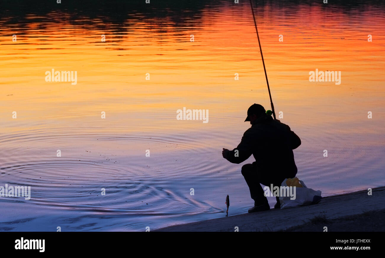 A fisherman fishing at sunset just caught a fish Stock Photo