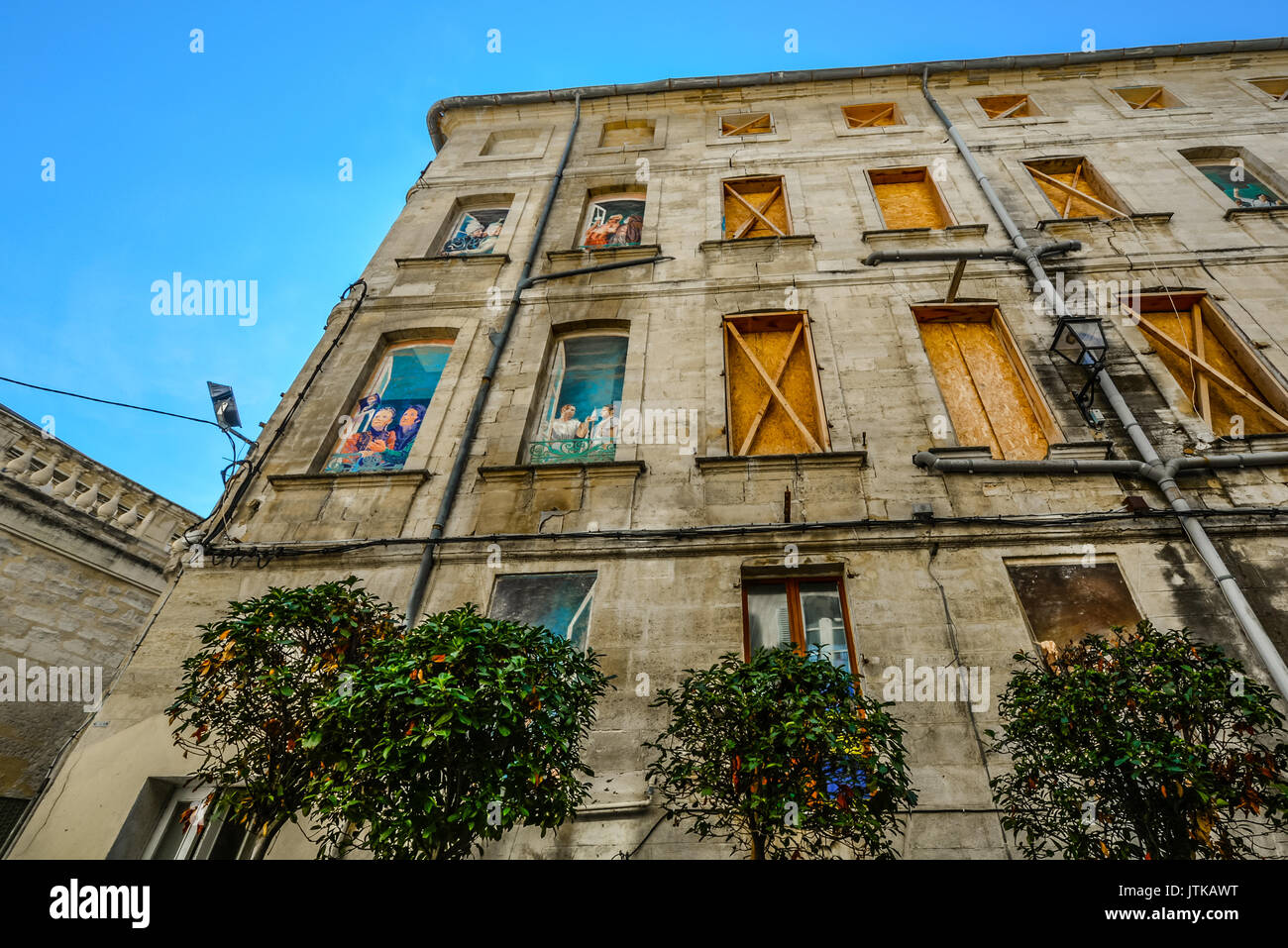 Old building in downtown Avignon France with boarded up windows and very colorfully painted scenes on the windows Stock Photo