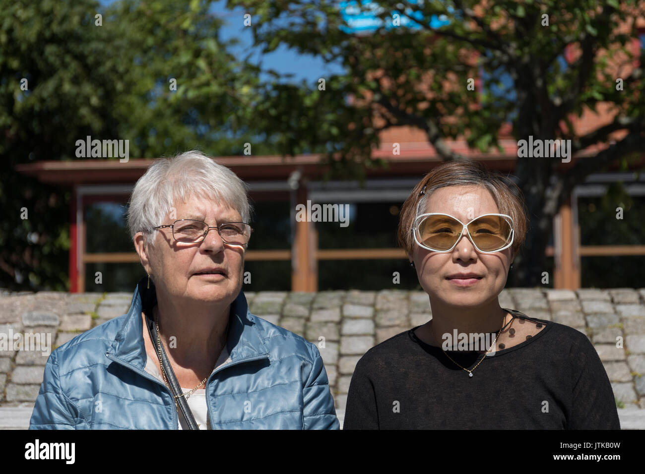 A Caucasian Swedish woman and her Taiwanese Chinese daughter-in-law sit next to each other on a sunny summer's day. Stock Photo