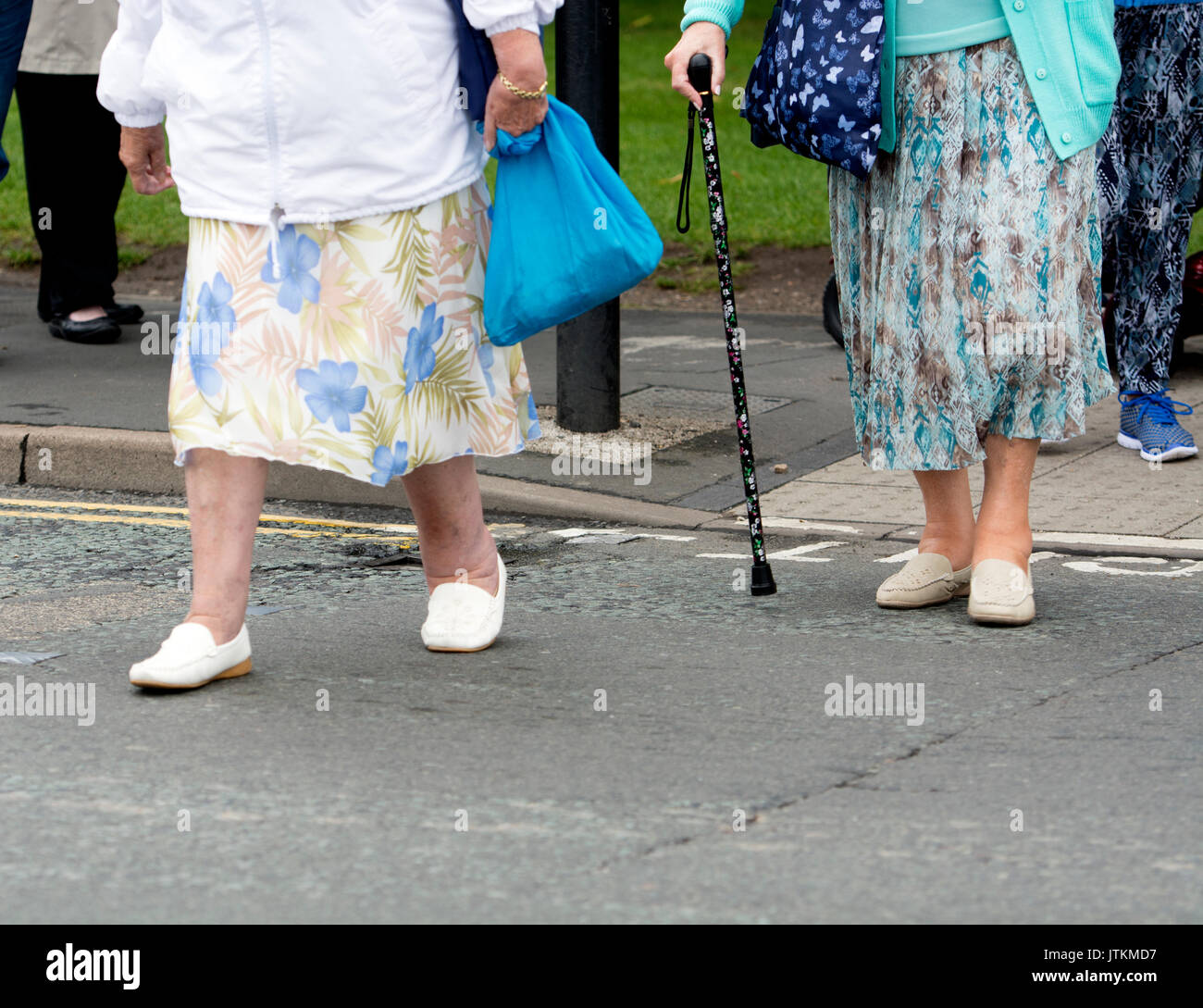 Two elderly women crossing a road at a pedestrian crossing, UK Stock Photo