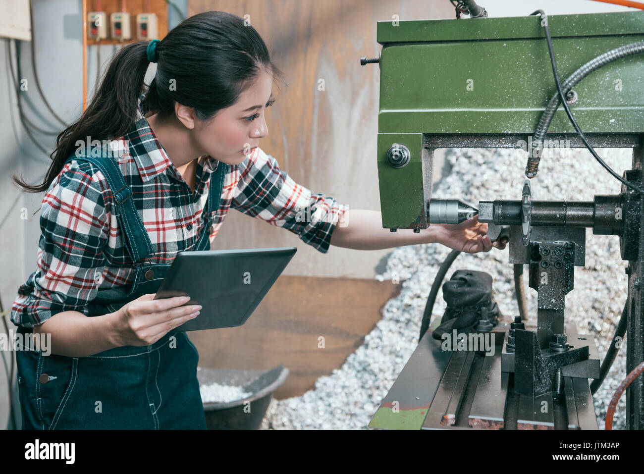 attractive pretty lathe worker manager holding mobile pad computer to checking working process and adjusting milling machine confirm product. Stock Photo