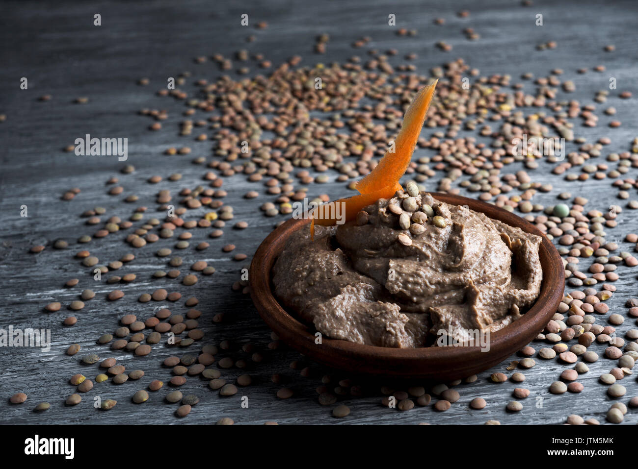 an earthenware bowl with appetizing lentil hummus on a rustic wooden table sprinkled with dried lentils Stock Photo
