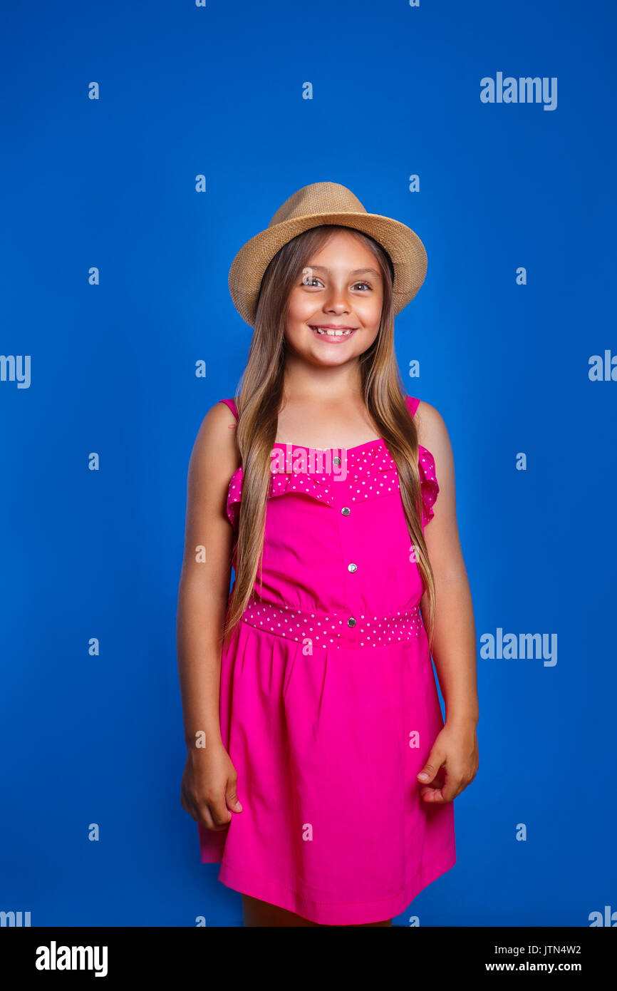 Cute little girl standing in pink jumpers and hat on the blue ...