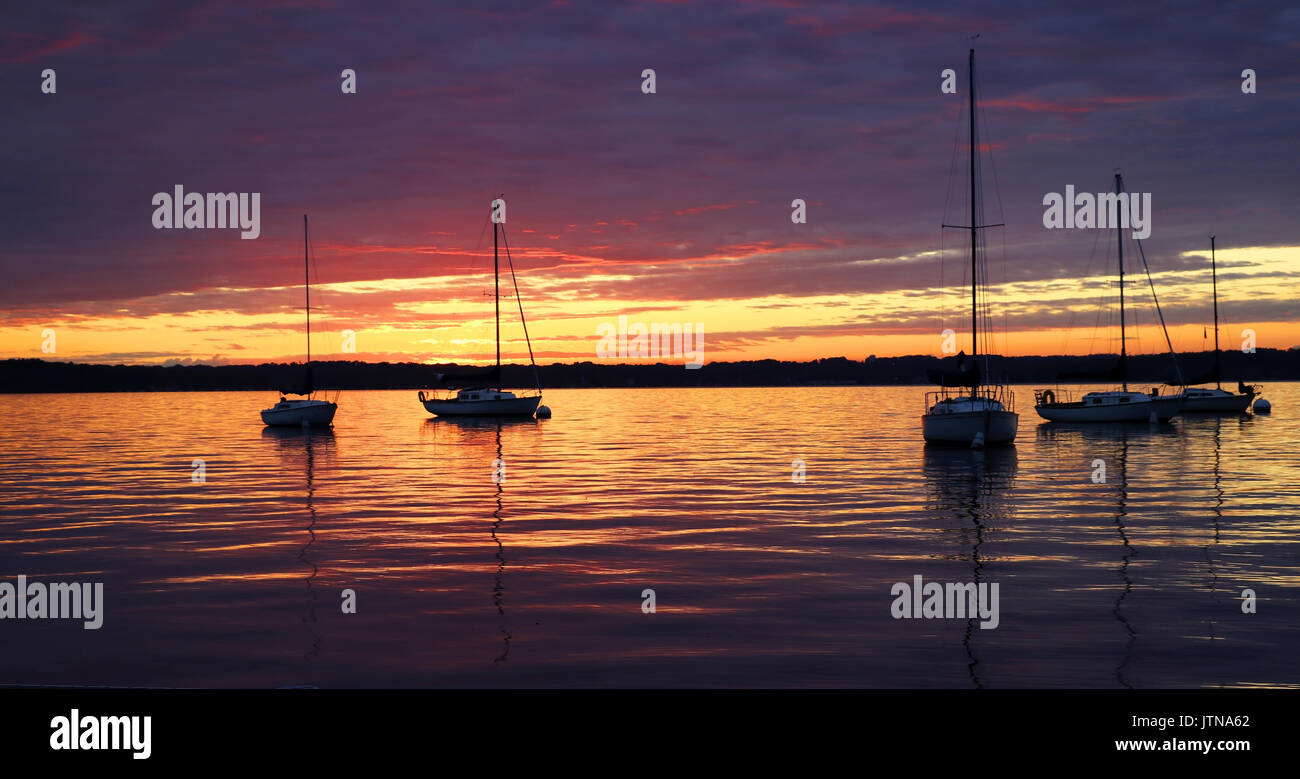 Amazing summer evening landscape with group of drifting yachts on a lake during spectacular sunset. Bright sky reflects in the lake water. Stock Photo