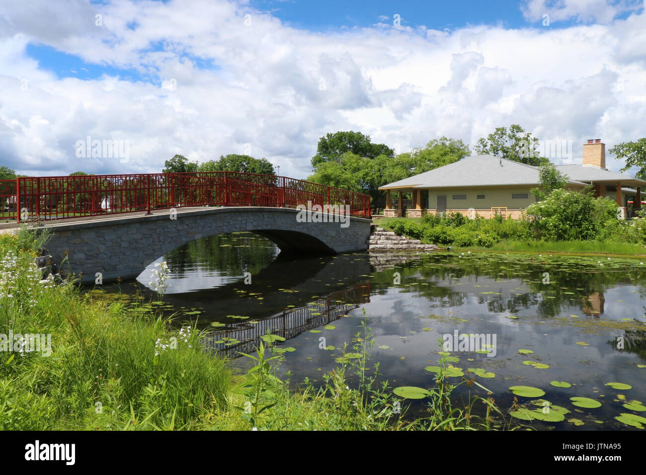 City park landscape with bridge reflected in the pond and beautiful cloudy sky at sunny day. Seasonal nature background. Stock Photo