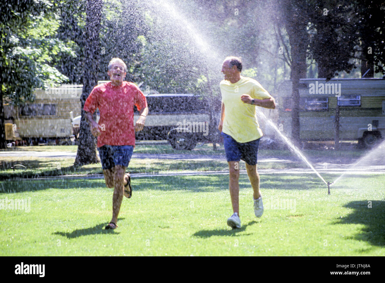 through sprinklers water playing arms stretched out loves life freedom abandonment careless worry free childlike playful joy joyful Myrleen Pearson Stock Photo
