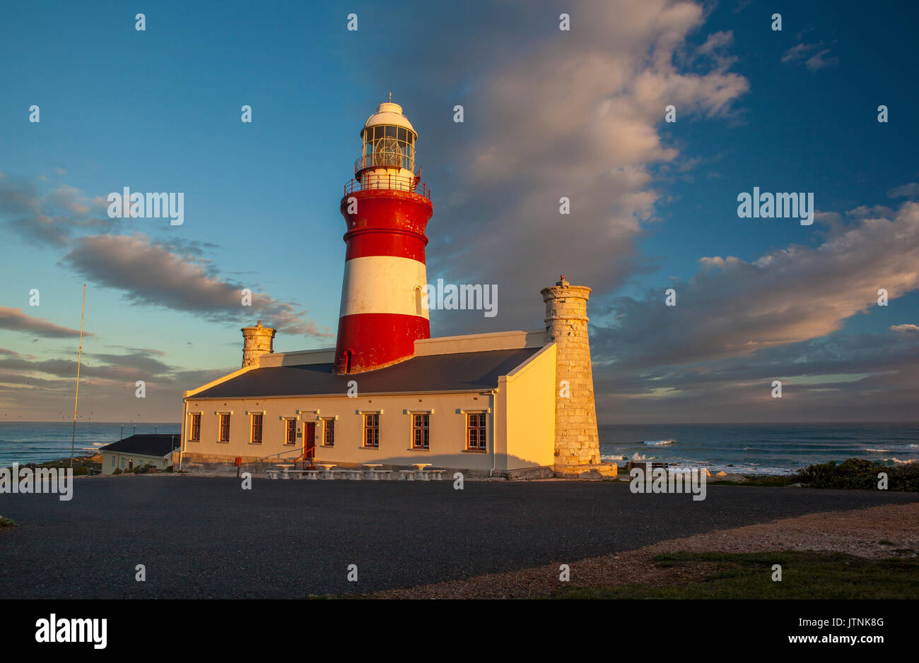 The historic 19th century lighthouse at Cape Agulhas, southernmost point of Africa, with its distinctive red tower and sandstone end towers at sunset Stock Photo