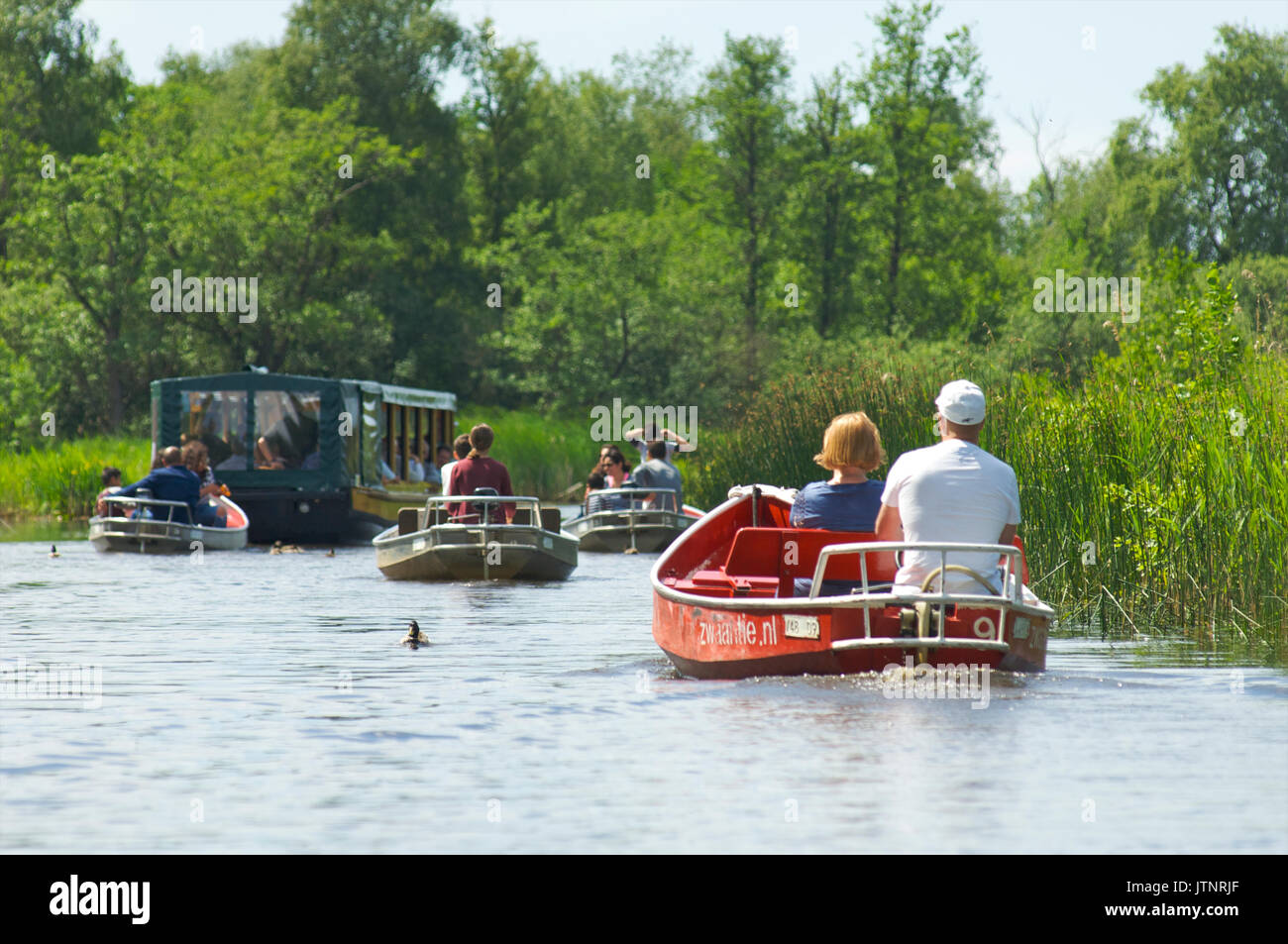 People in rental boats sailing together down a canal on their way to lake Bovenwijde near Giethoorn Stock Photo