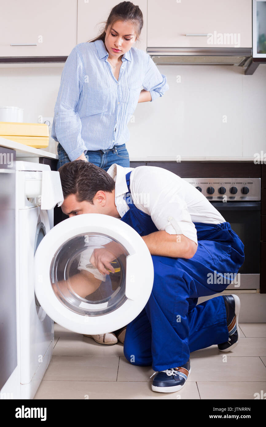 Young woman and professional mechanic repairing broken washing machine at home kitchen Stock Photo