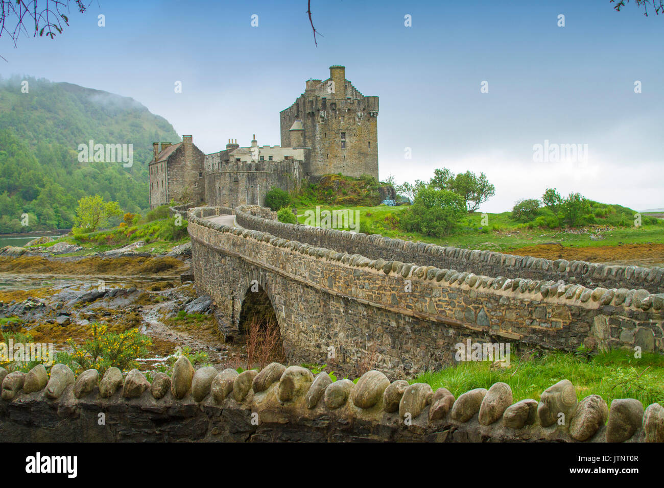 View of spectacular Eilean Donan castle and bridge across loch against blue sky and mist in Scotland Stock Photo