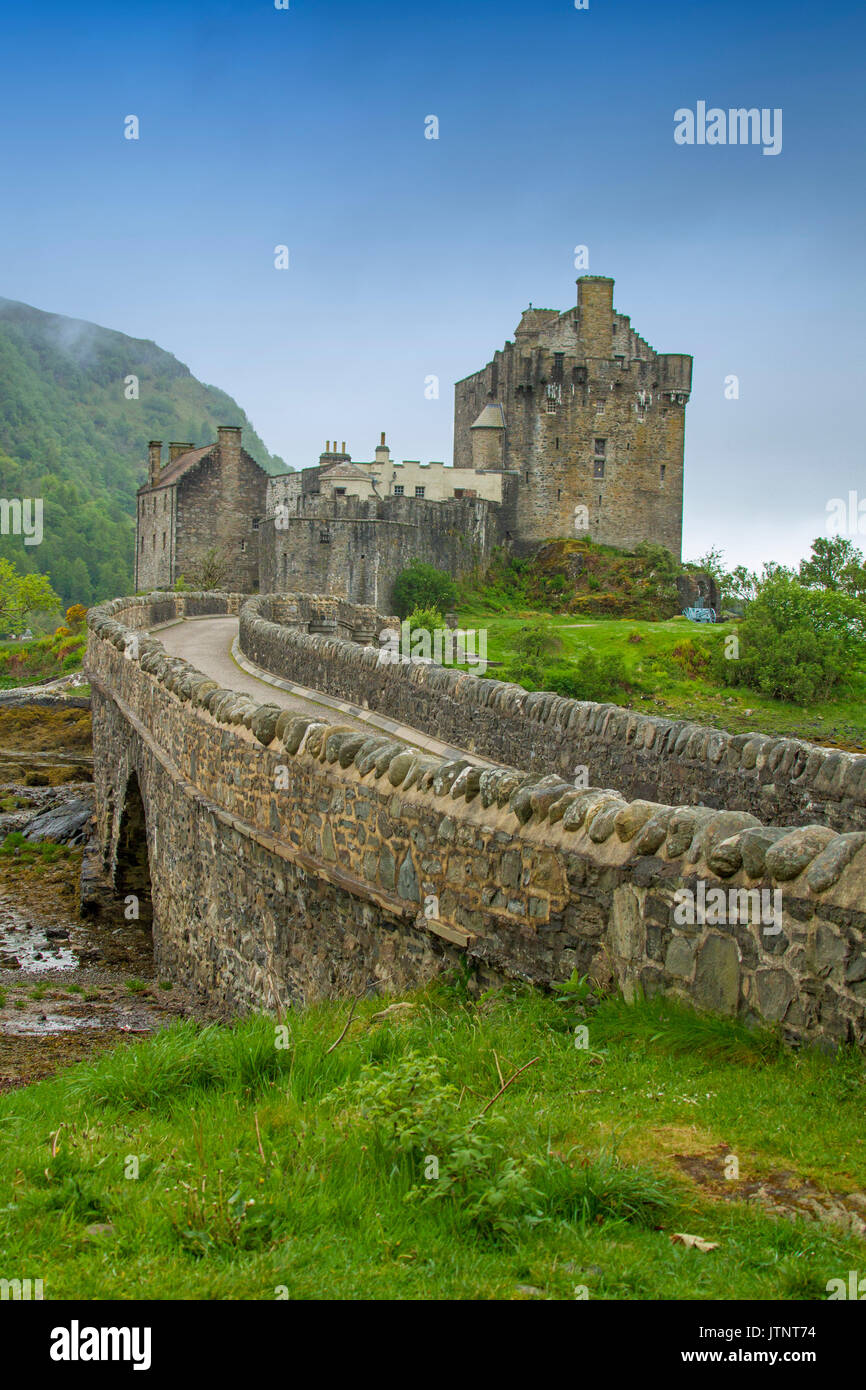 View of spectacular Eilean Donan castle and bridge across loch against blue sky and mist in Scotland Stock Photo